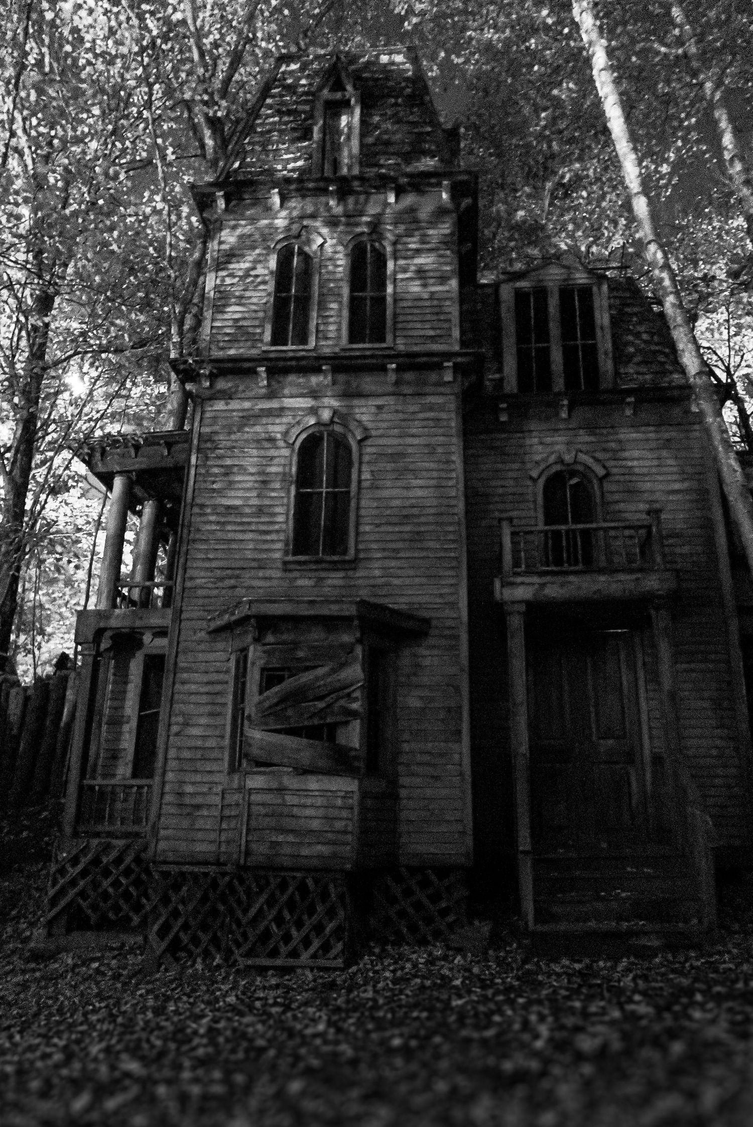 Eerie black and white photo of an abandoned Victorian haunted house surrounded by bare trees.