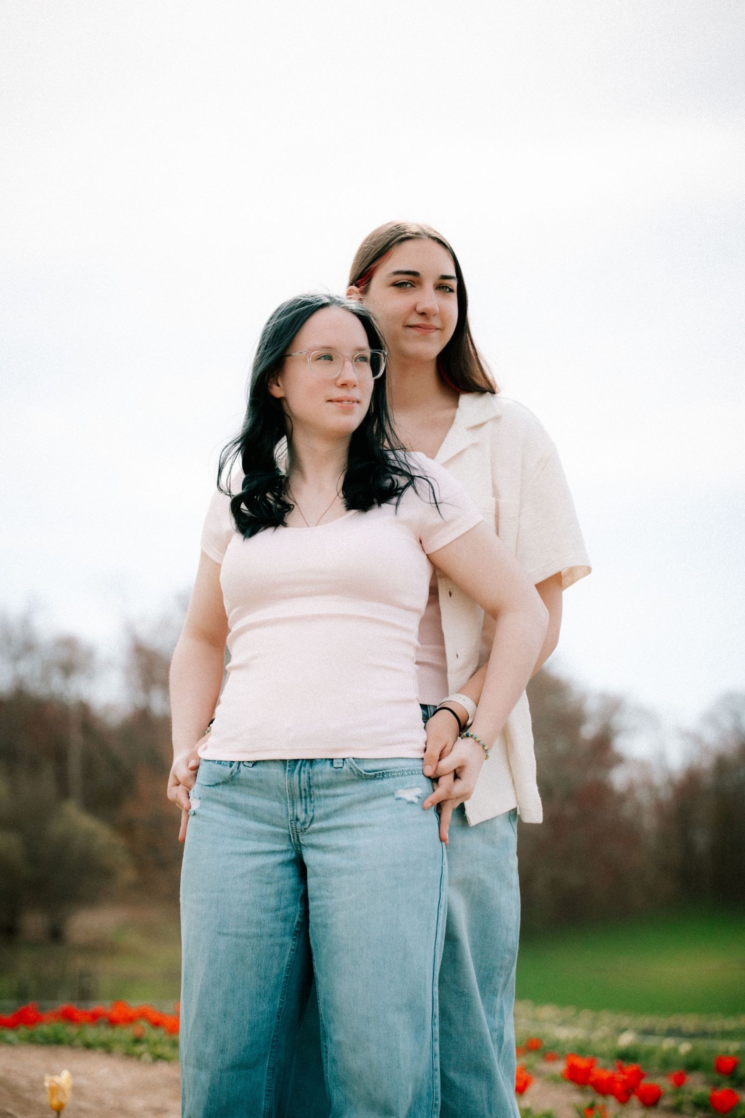 Two young women standing together in a field with red tulips in the background.