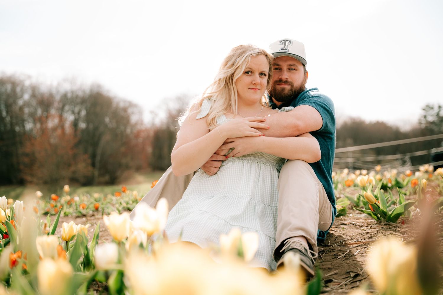 A loving couple sits together embracing in a colorful tulip field during a romantic spring engagement session.
