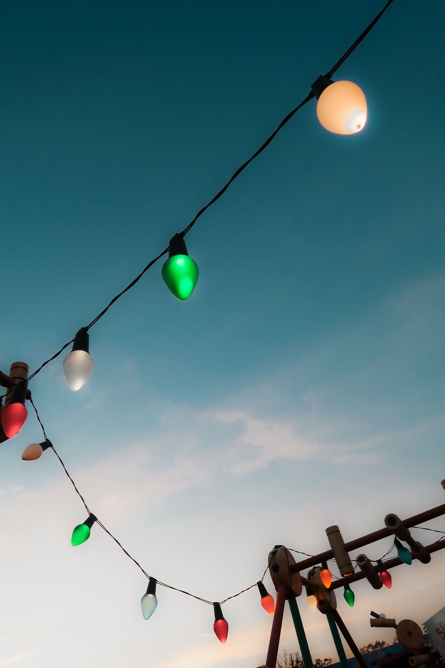 Colorful Christmas string lights hang against a twilight blue sky at dusk.