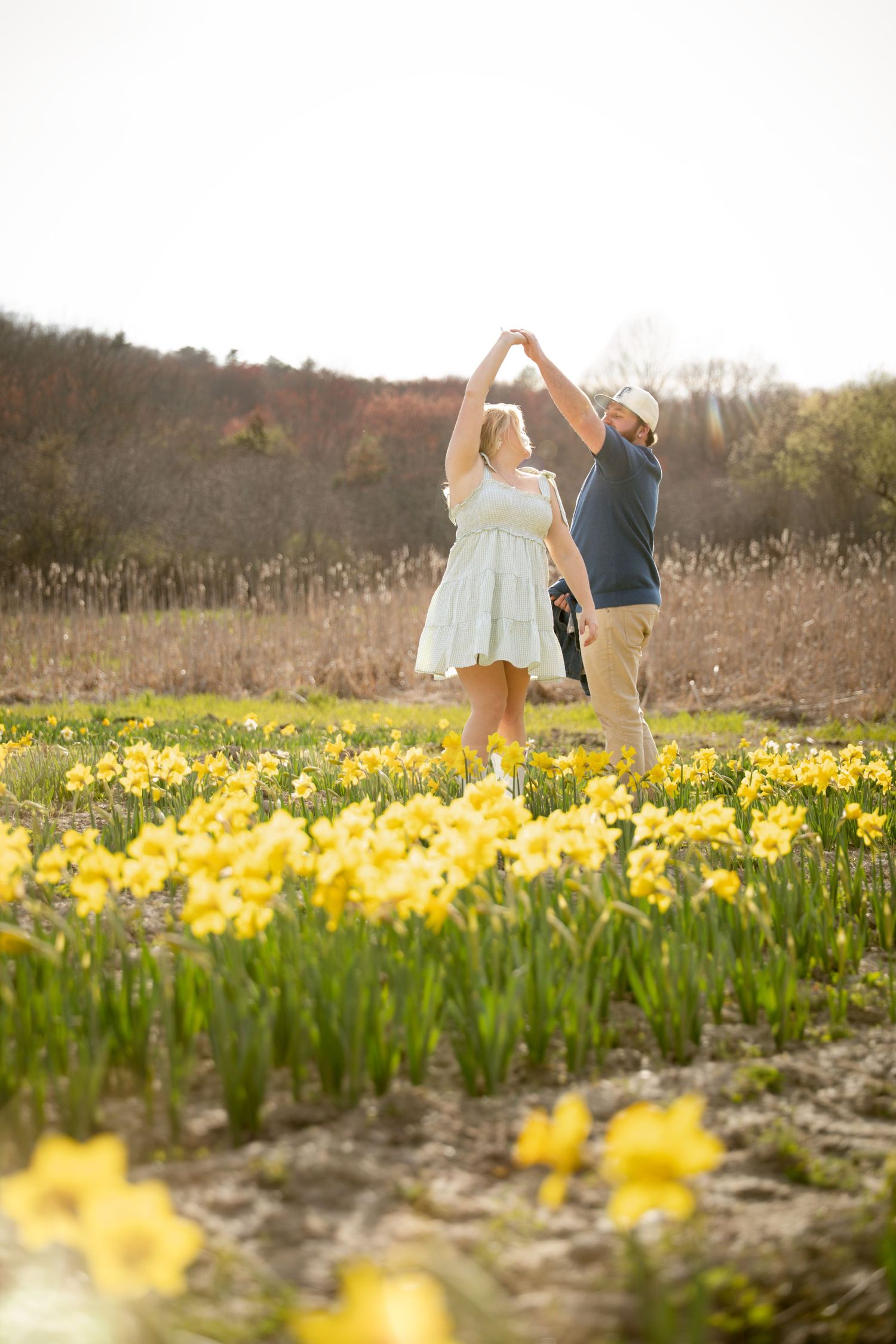 Couple dancing and twirling together in a sunny field of yellow daffodils in spring.