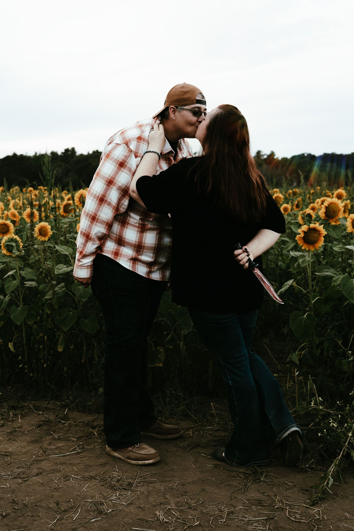 Couple kissing in front of a lush sunflower field at dusk.