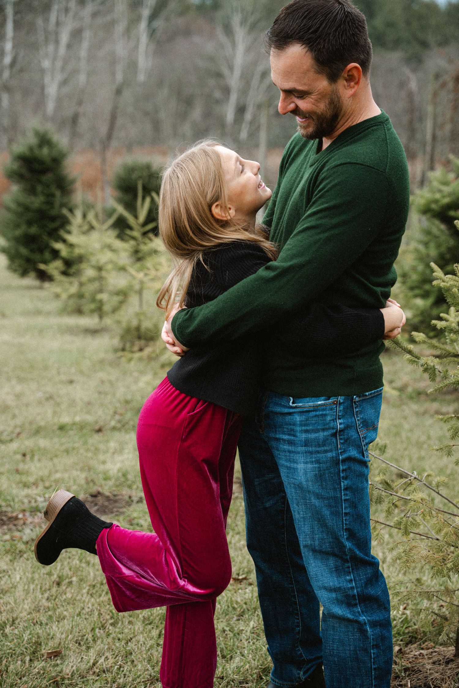Father and daughter hugging and laughing together in a Christmas tree farm field.