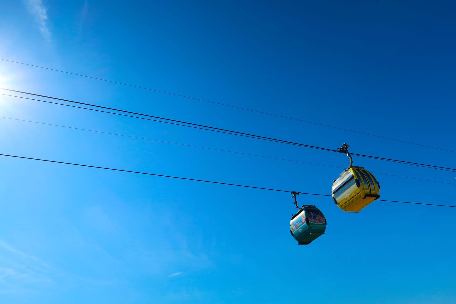 Two colorful cable car gondolas suspended on wires against a bright clear blue sky on a sunny day.