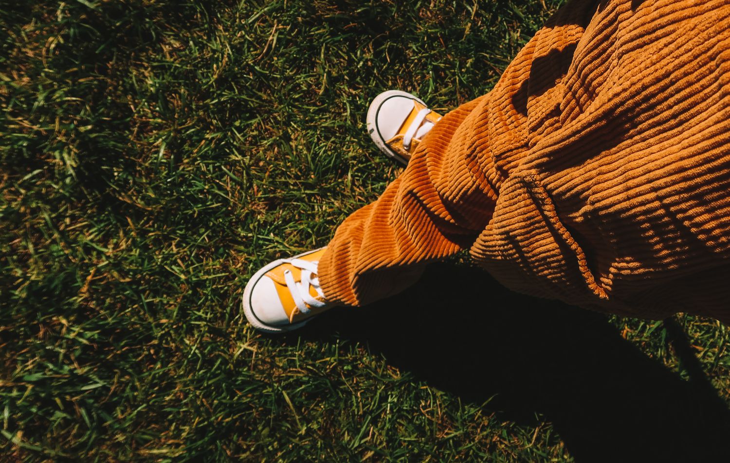Person wearing orange corduroy pants and yellow Converse sneakers standing on green grass.