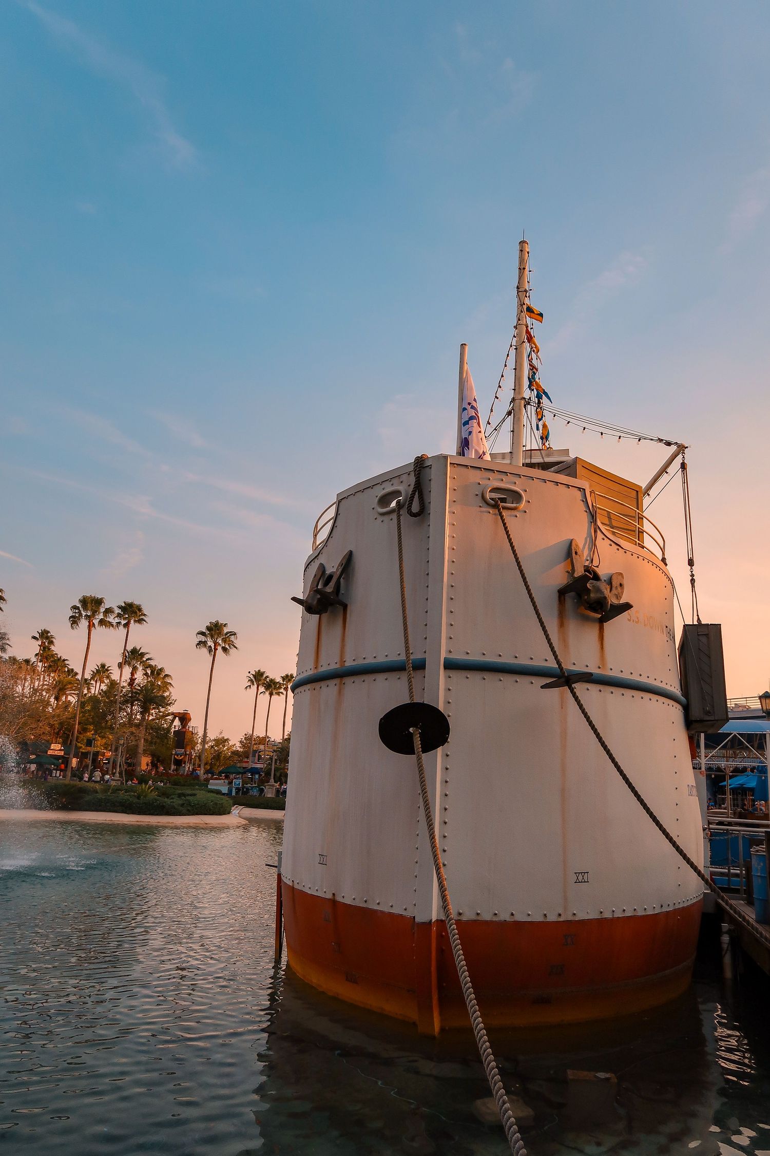 A vintage white and orange tugboat docked at sunset with palm trees and calm water reflecting golden light.