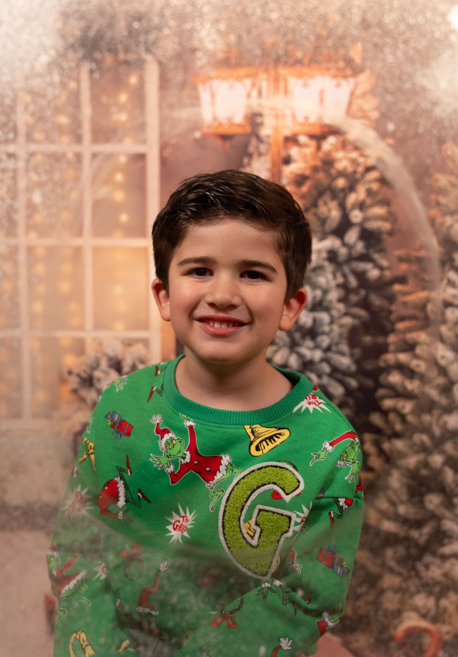 Happy boy in green Grinch sweater smiling at Christmas backdrop.