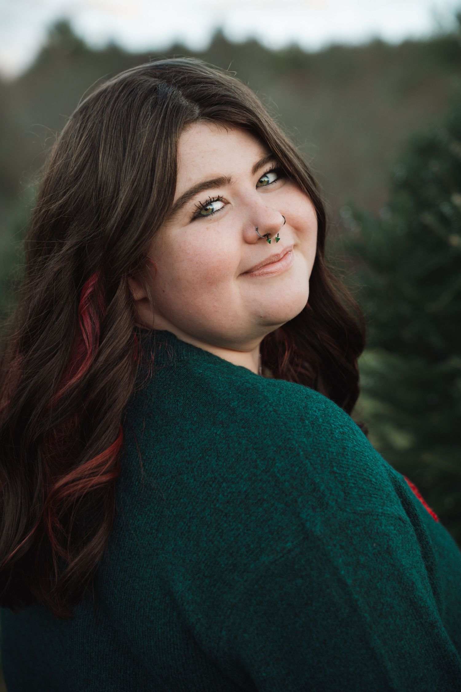 Young woman with nose ring smiling at Christmas tree farm.