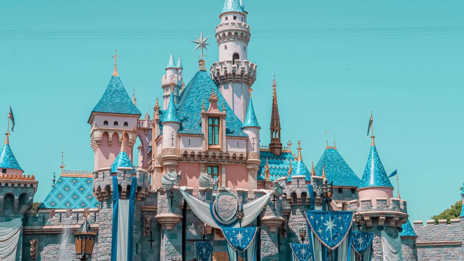 Iconic Sleeping Beauty Castle at Disneyland with blue and pink turrets against a clear sky.