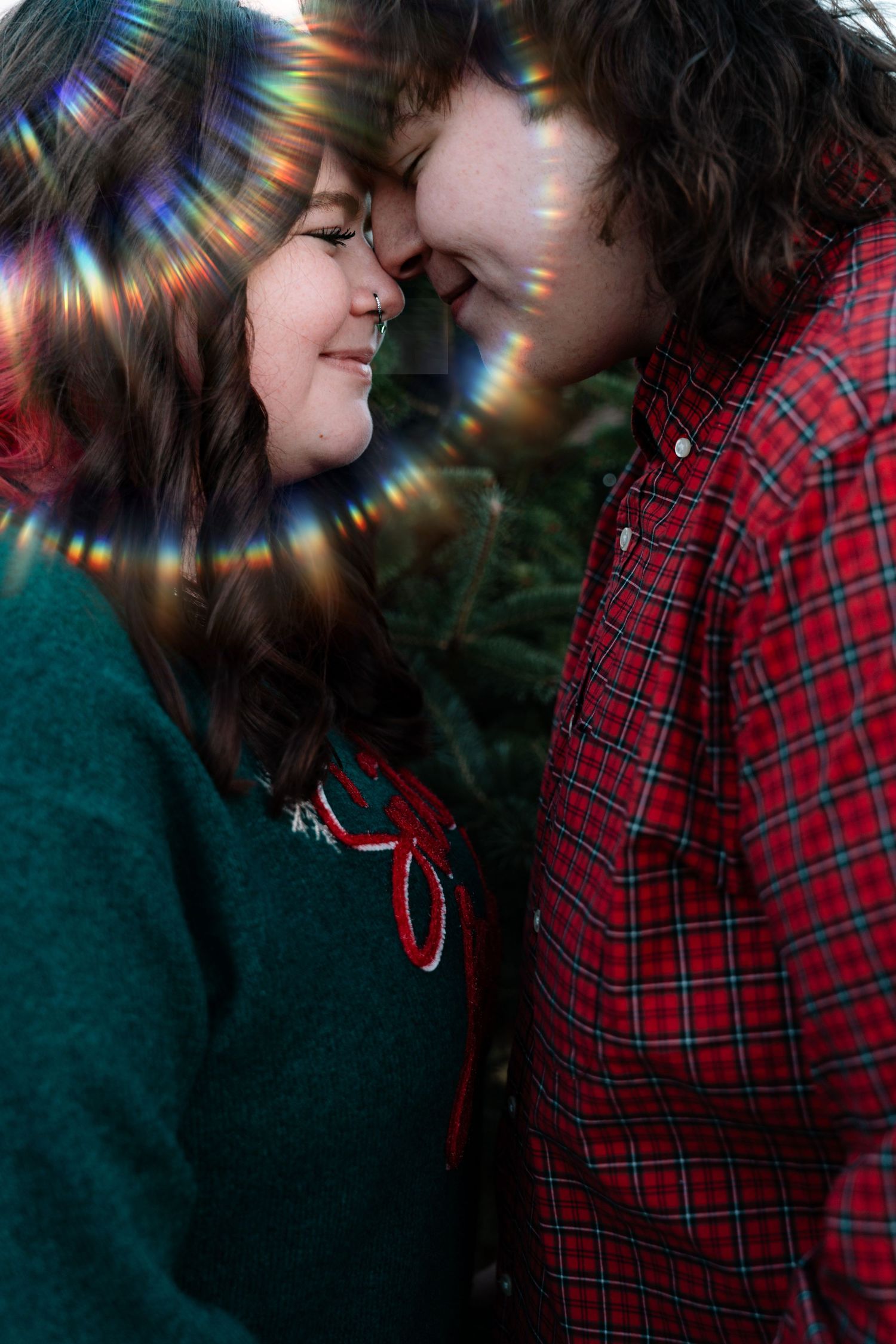 A young couple shares a close romantic moment touching foreheads near a Christmas tree with bokeh light effects.