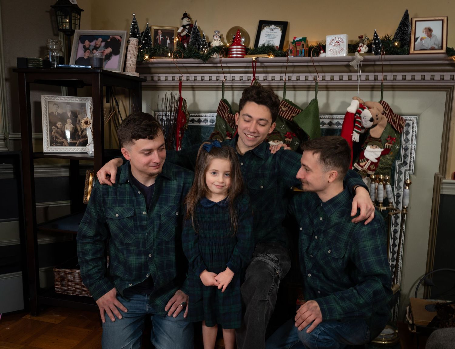 Three brothers and a young girl in matching plaid shirts posing by a Christmas fireplace.