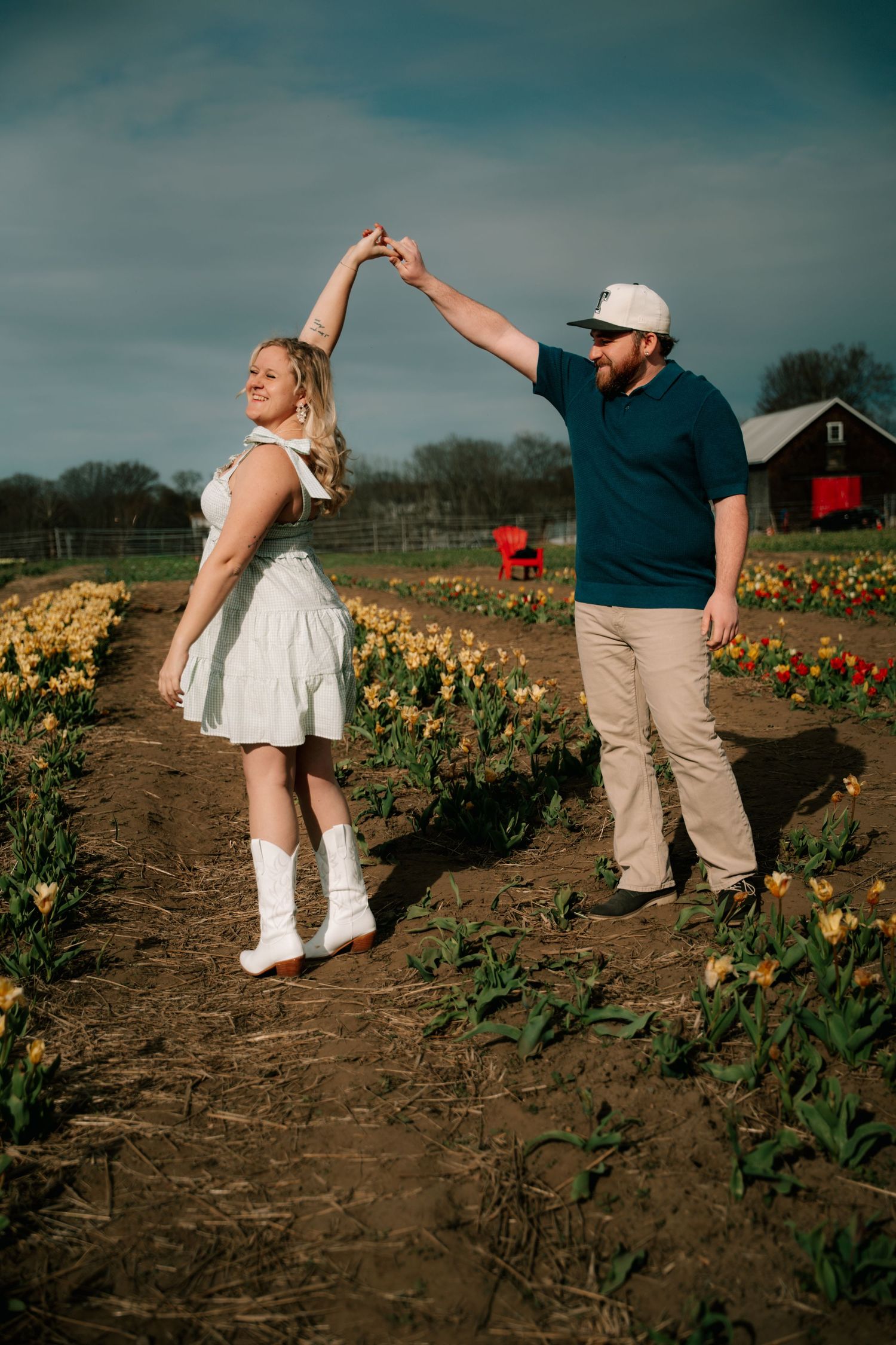Happy couple dancing together on a dirt path between rows of colorful tulips on a farm.