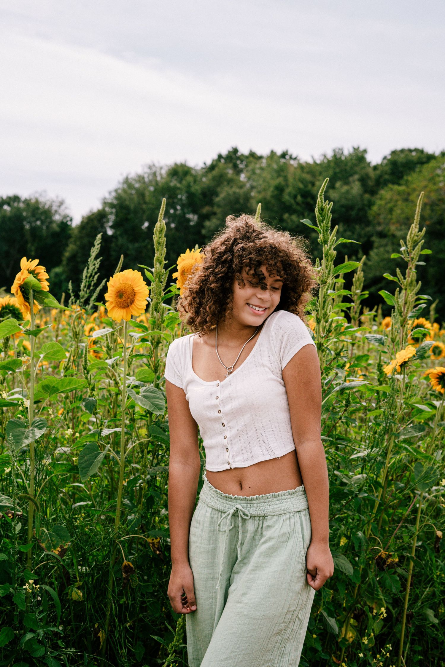 Smiling young woman with curly hair standing in sunflower field.