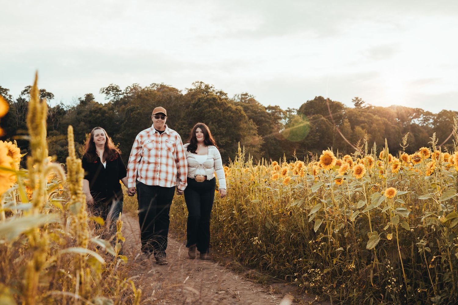 Family of three walking along a sunlit sunflower field path.