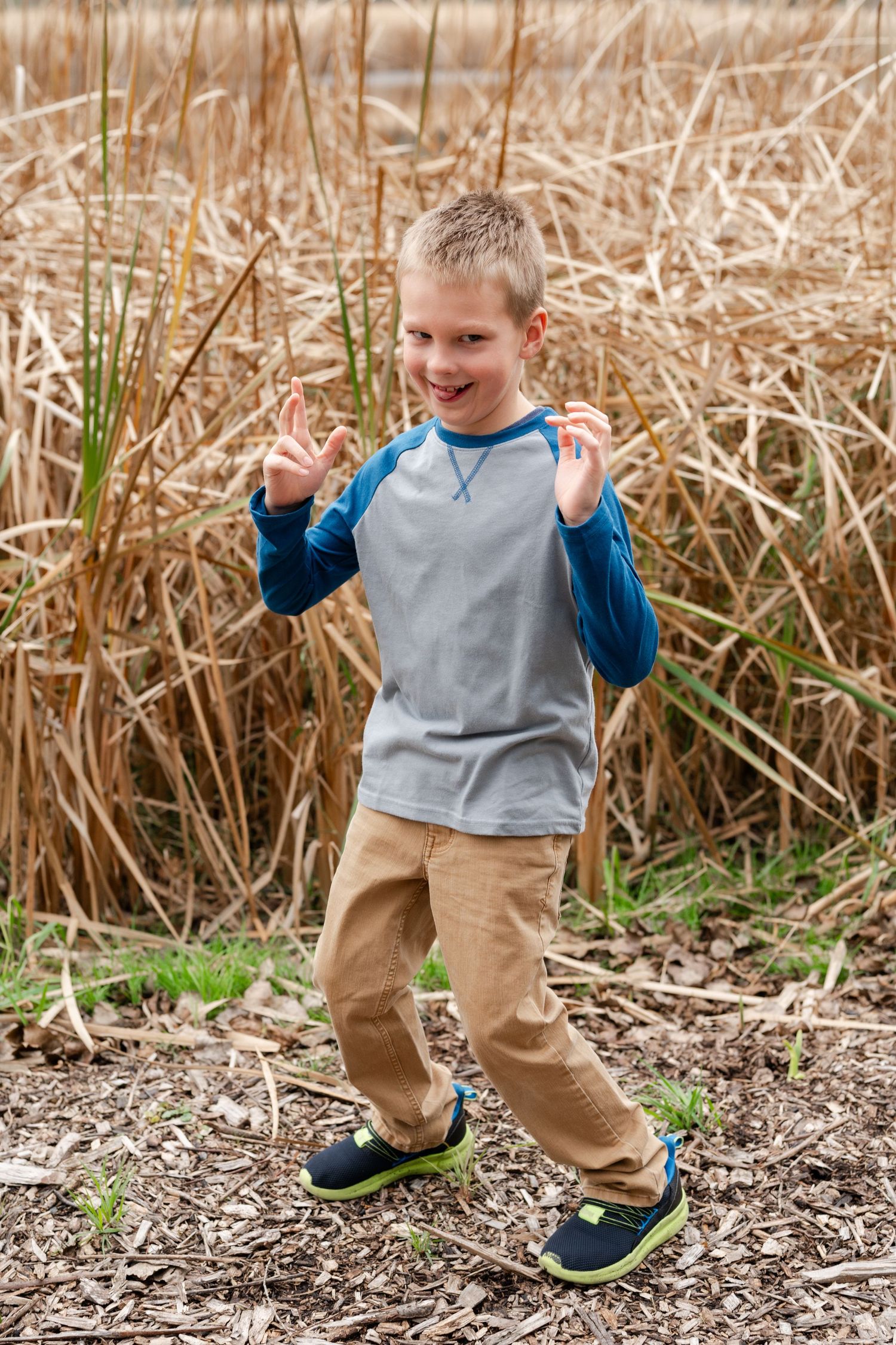 Child in gray and blue raglan shirt dancing joyfully on a nature path.