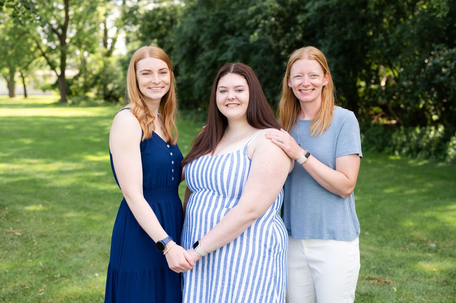 Three women in coordinated outfits smile together during an outdoor photo session.