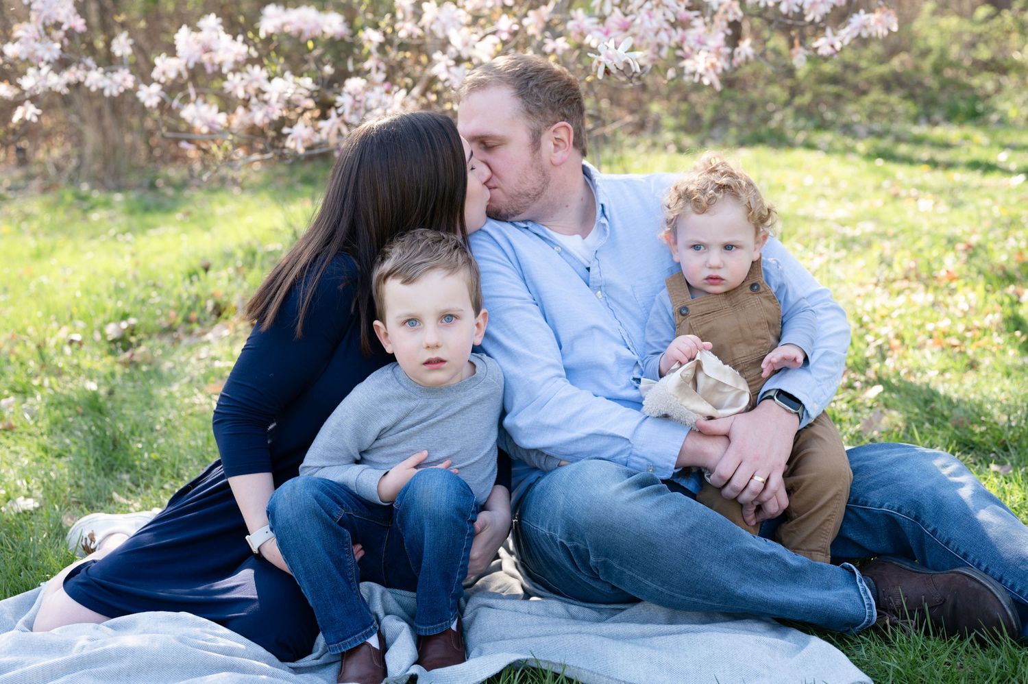 Intimate family moment on picnic blanket surrounded by blooming spring trees.