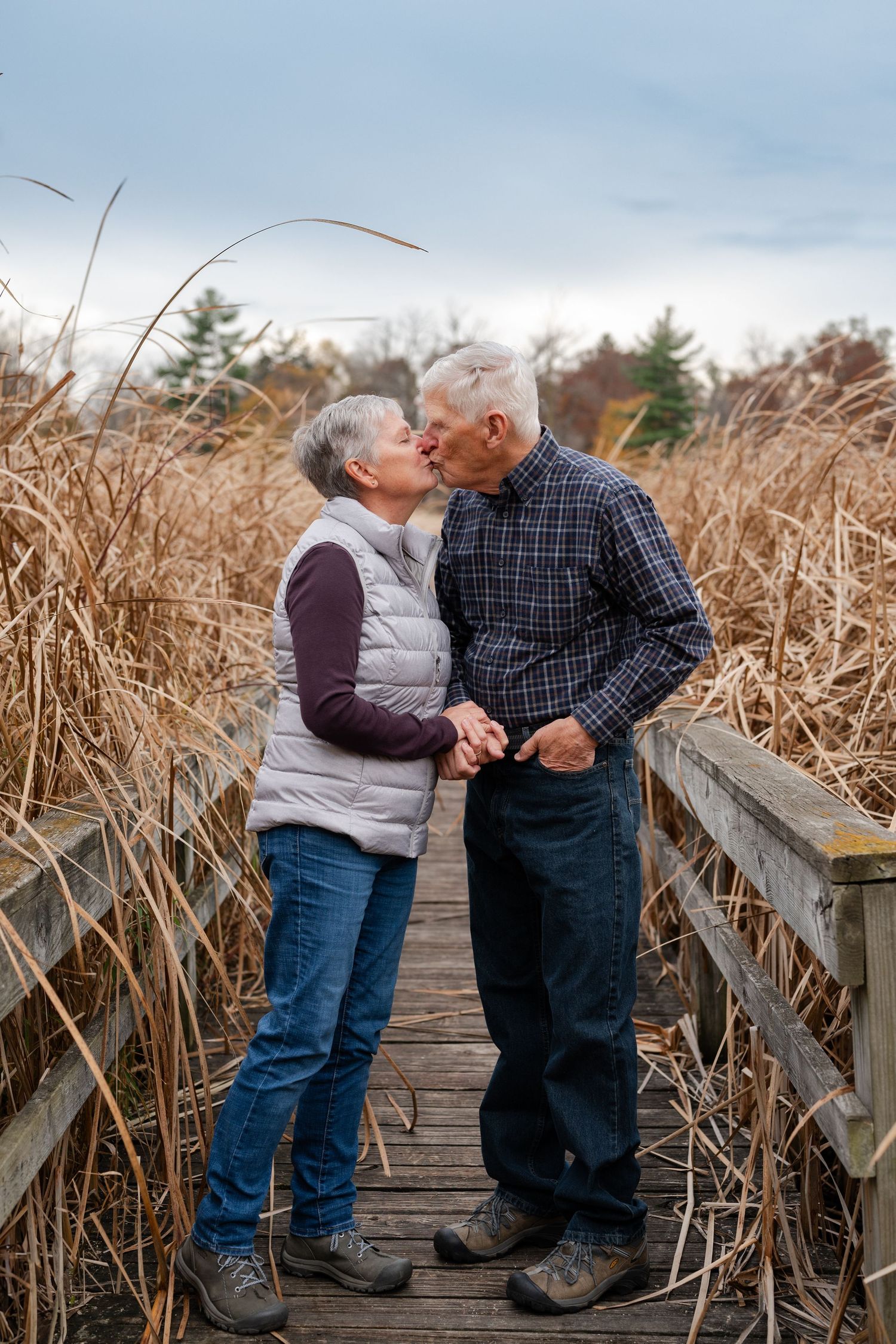 Romantic moment shared between couple on wooden boardwalk surrounded by dried reeds.
