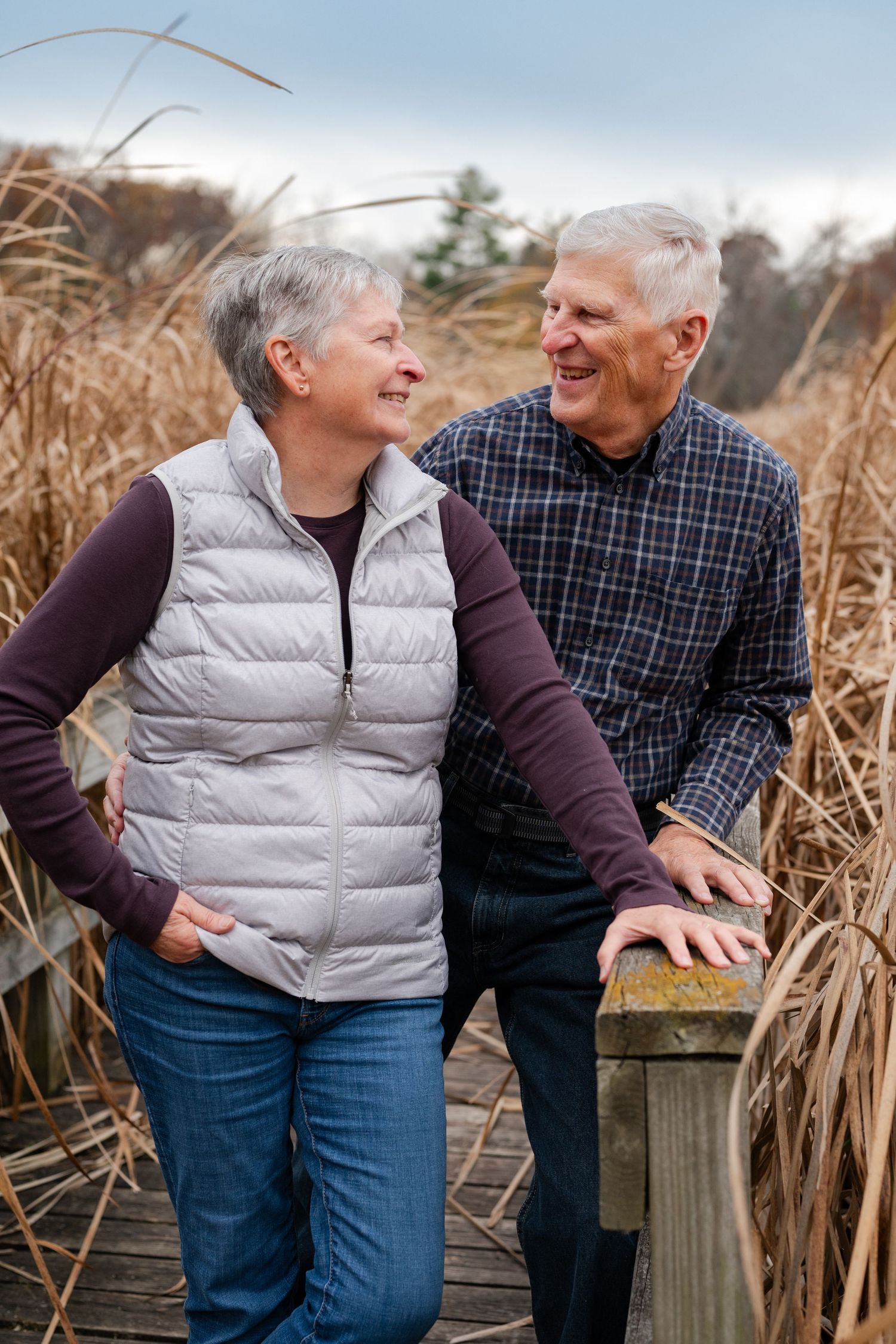 Mature couple shares a tender moment on a wooden boardwalk surrounded by tall autumn grasses.