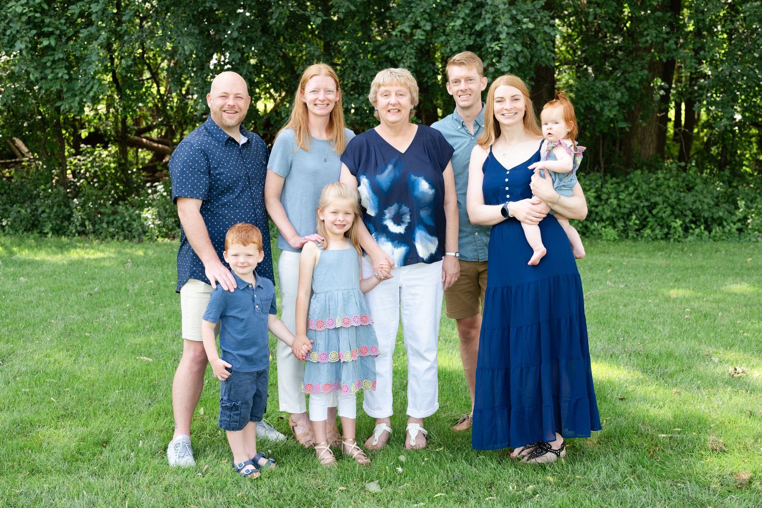 Extended family group portrait outdoors with adults and children in coordinated blue and white outfits.