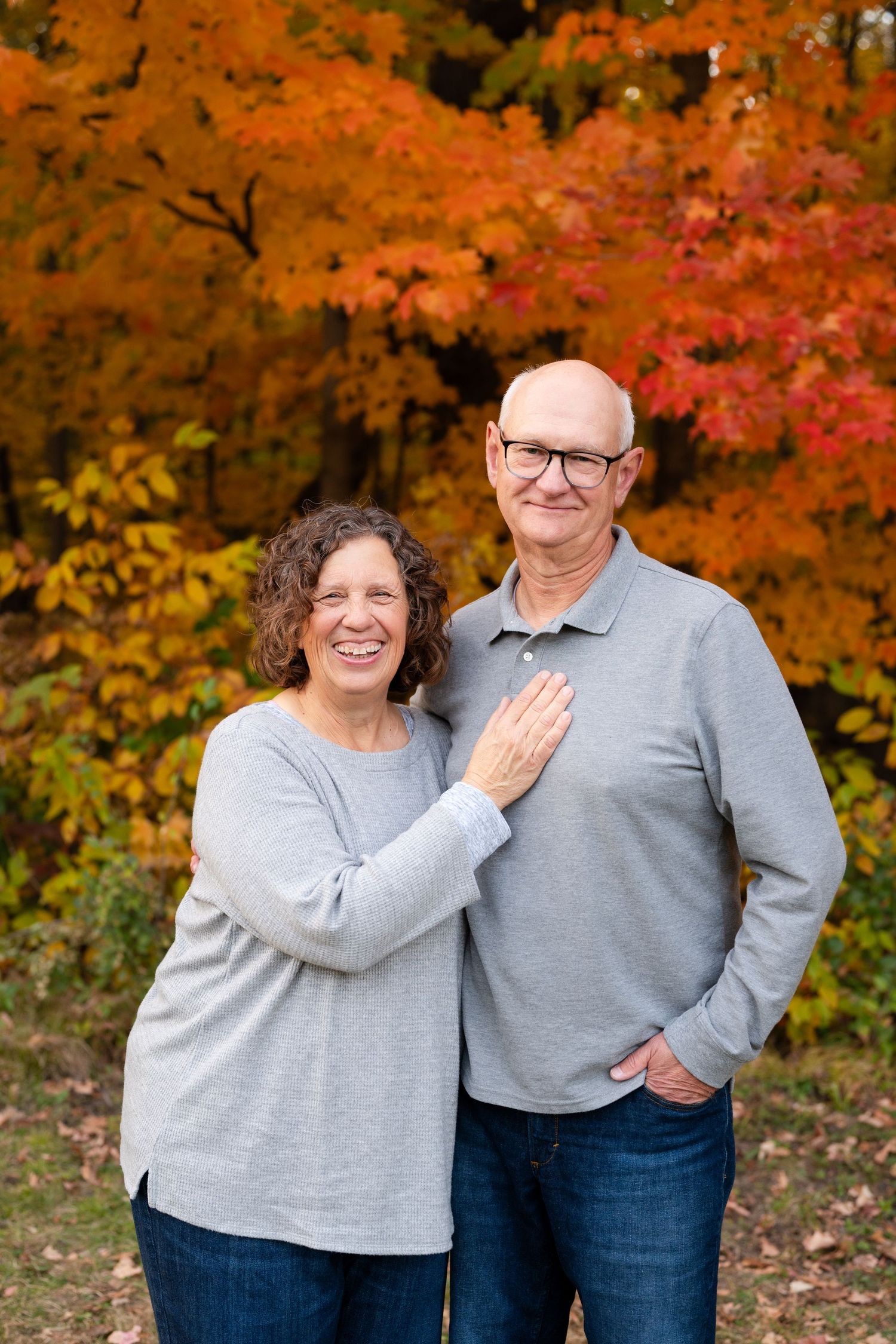 Happy couple embraces against vibrant autumn foliage with brilliant orange maple leaves in the background.