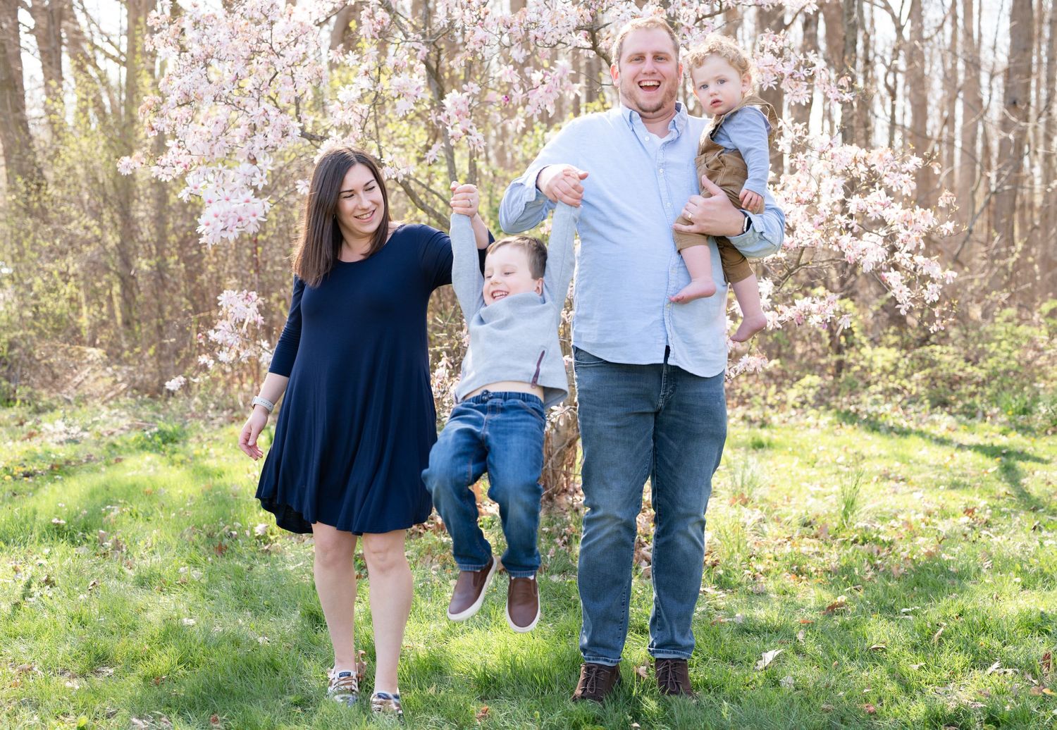 Dynamic family photo with playful jumping pose under spring blossoms.