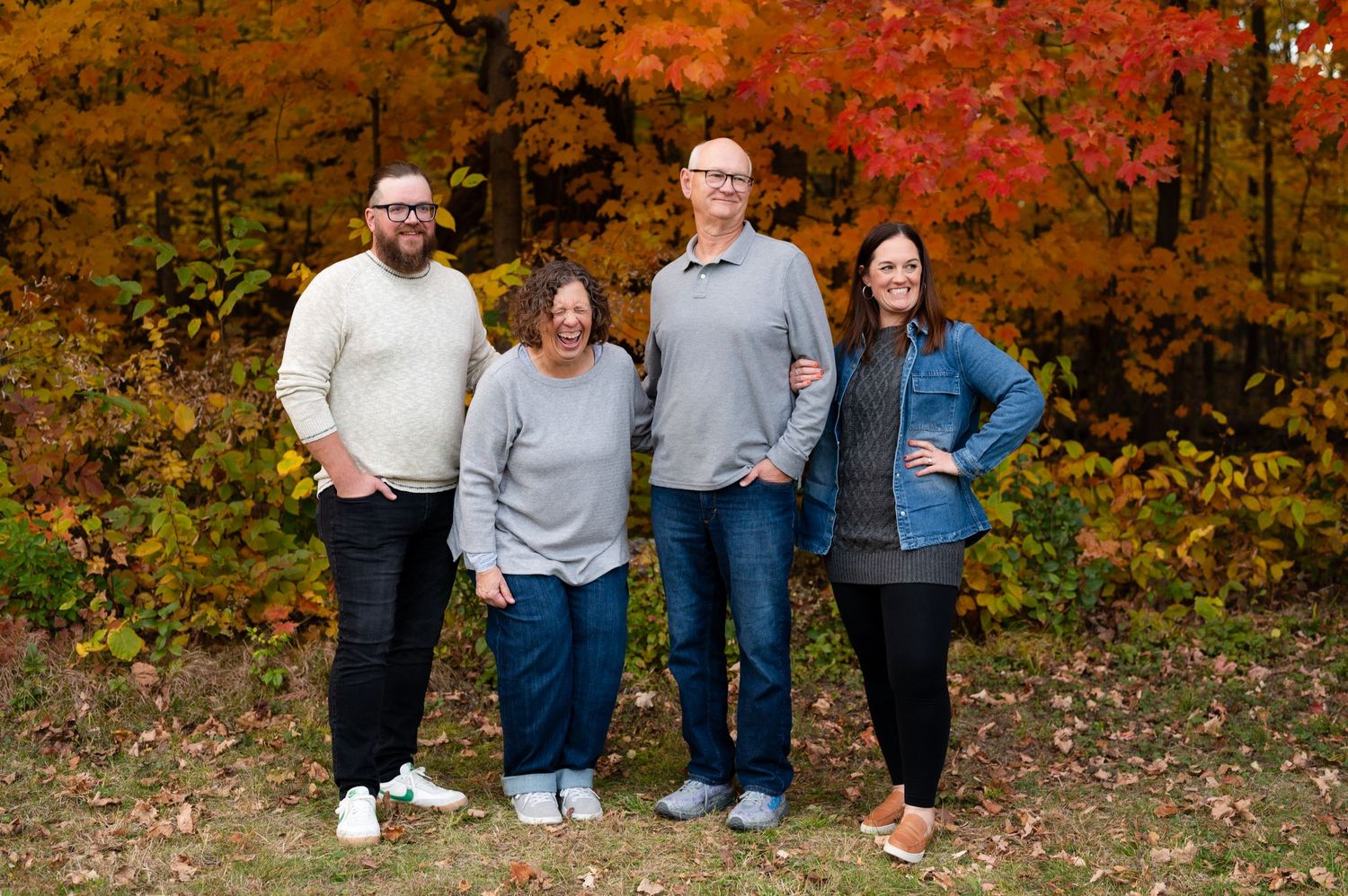 Four people standing together outdoors with brilliant autumn colors behind them.