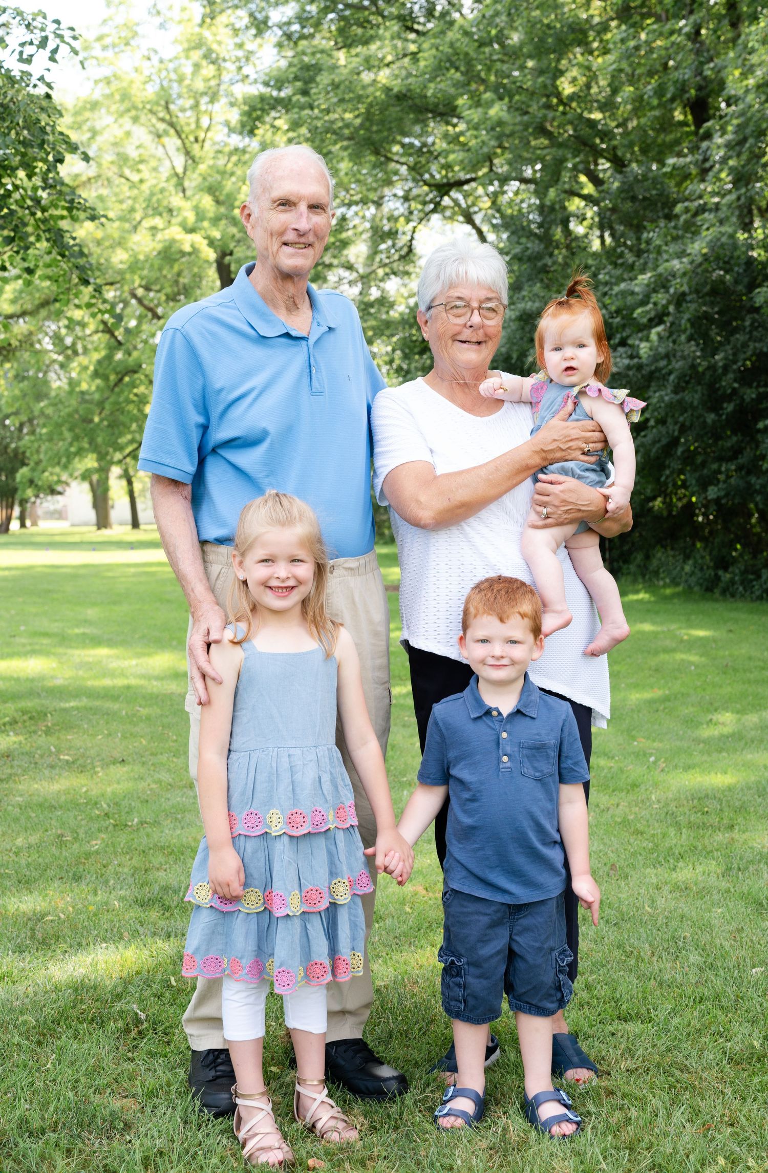 Family group portrait taken outside with three generations together in a park setting.
