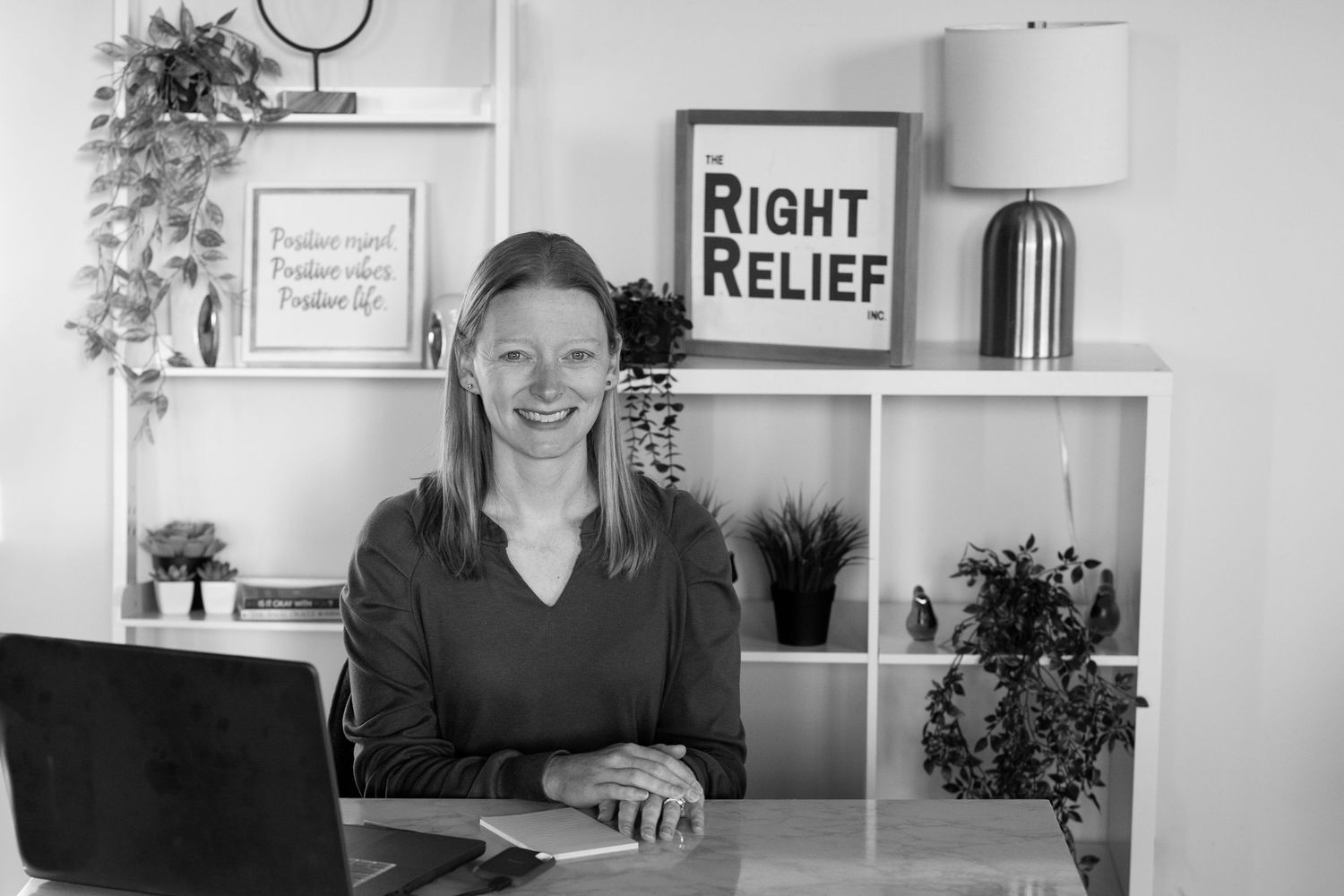 Office workspace with white shelving unit displaying plants, decor and a Right Relief sign.