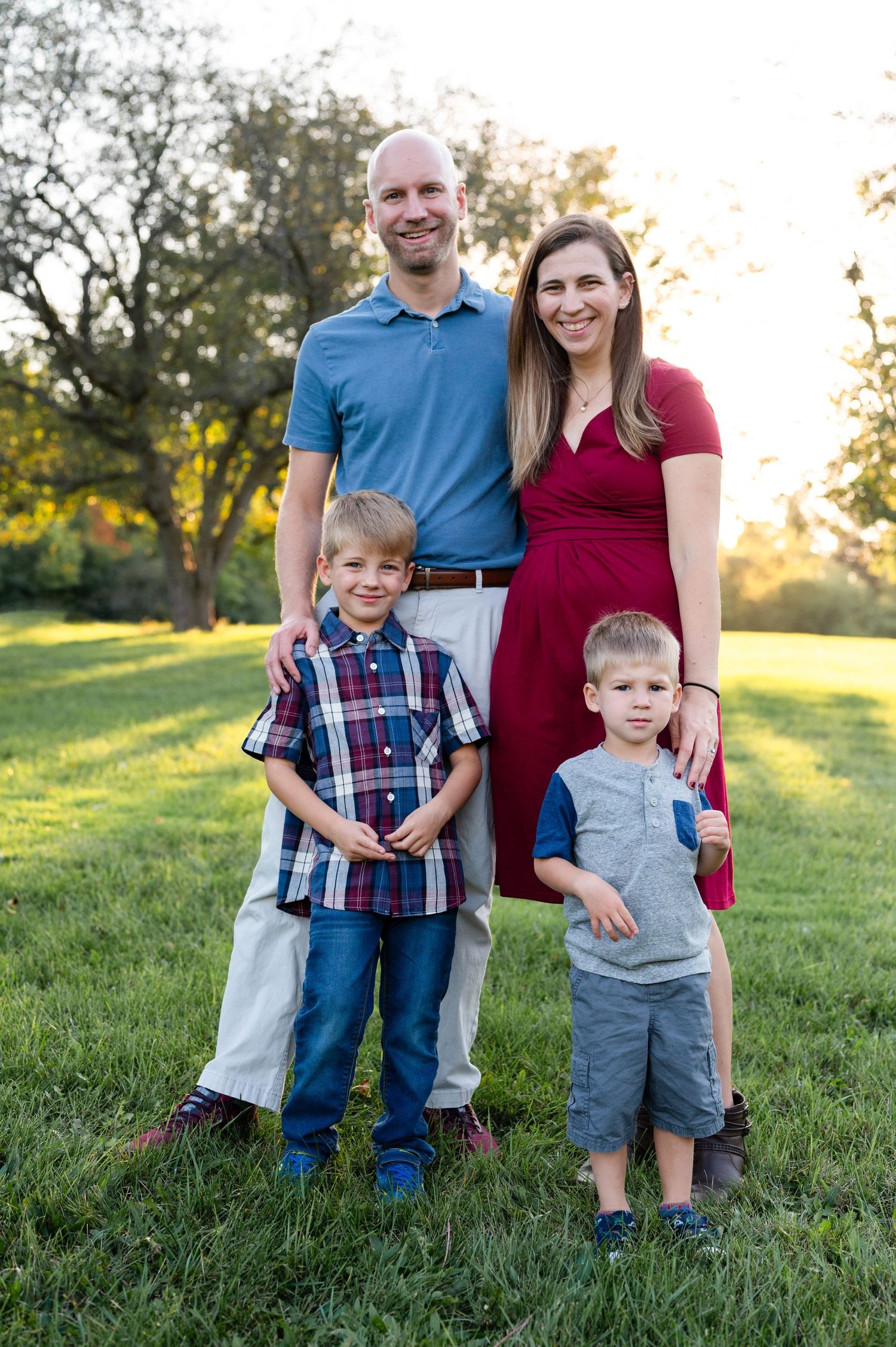 A family of four poses together on a grassy hill during golden hour.