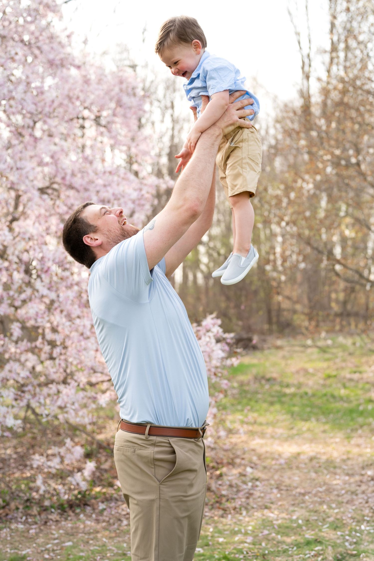 A joyful moment captured outdoors with cherry blossoms as someone lifts a small child high into the air.