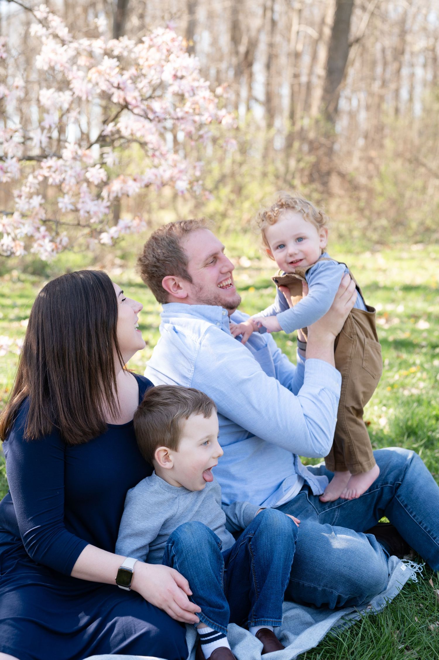 Candid family moment captured on a blanket surrounded by blooming spring flowers in a park setting.