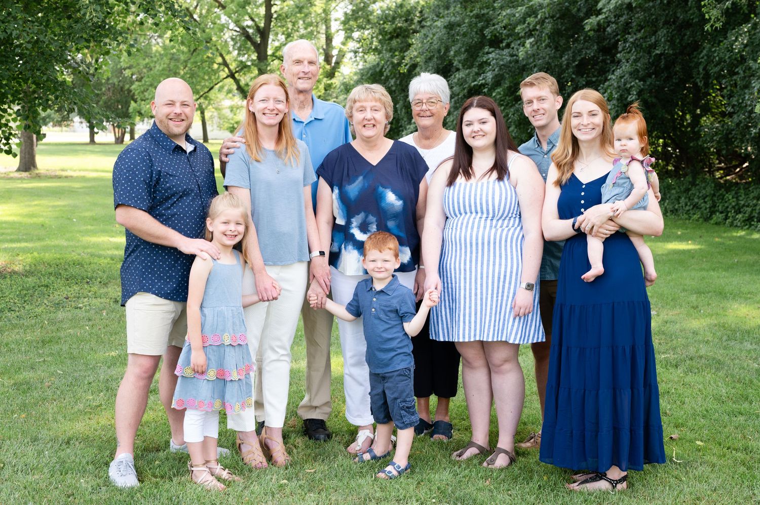 Large family gathering outdoors with multiple generations posing together in a park setting.
