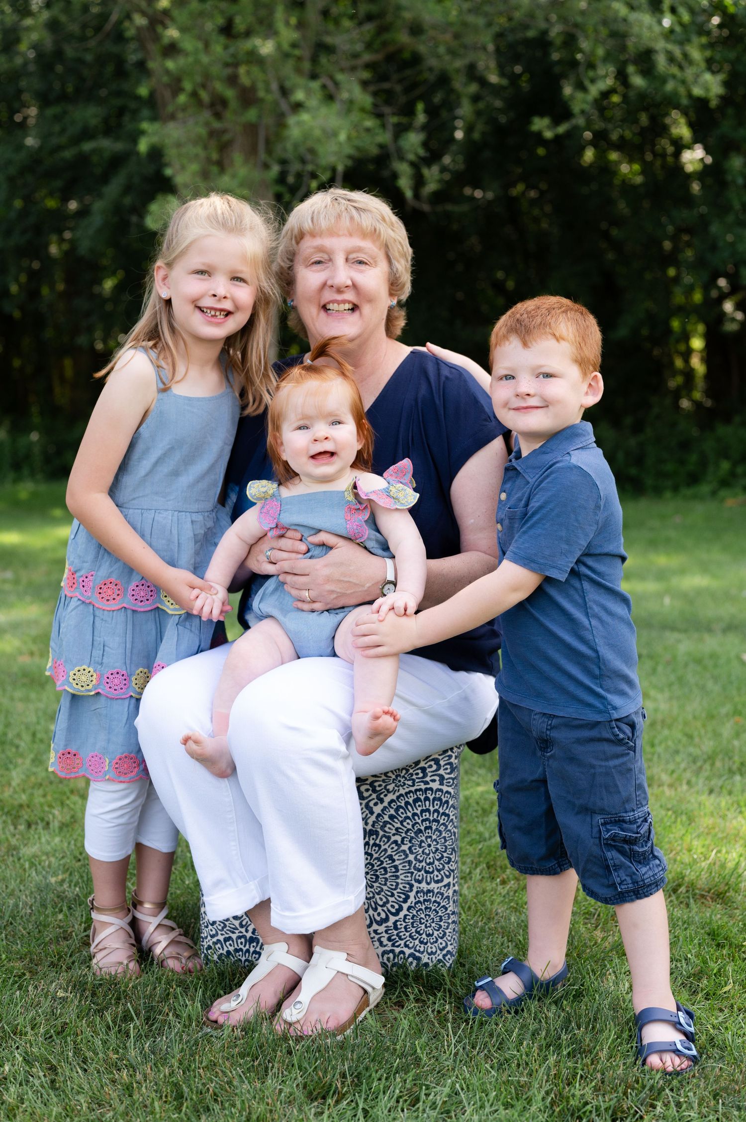 Four family members share joyful laughter while sitting together on grass outdoors.