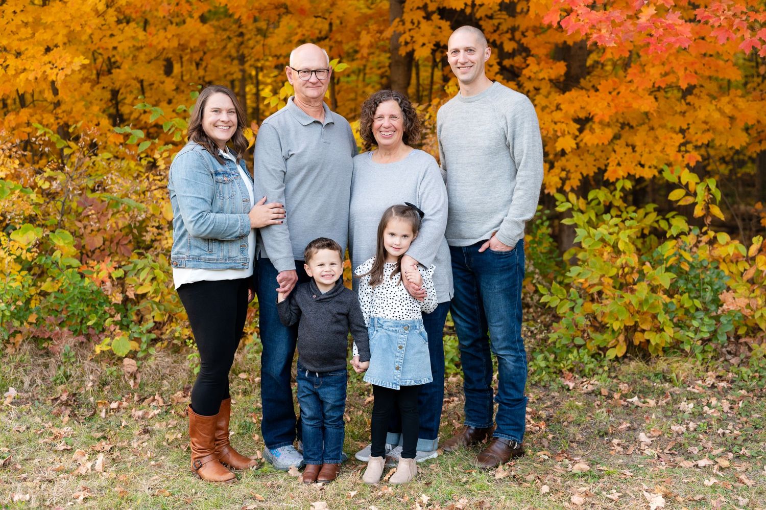 Extended family poses together for outdoor portrait with stunning fall colors behind them.