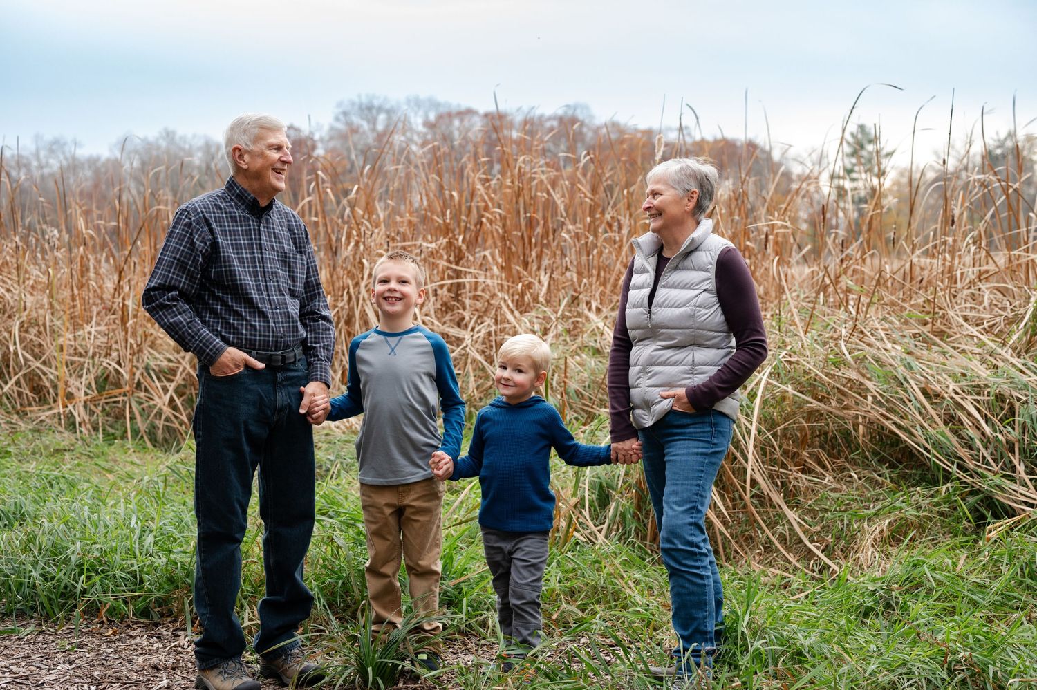 Four people enjoying an outdoor moment together among tall grass and autumn foliage.