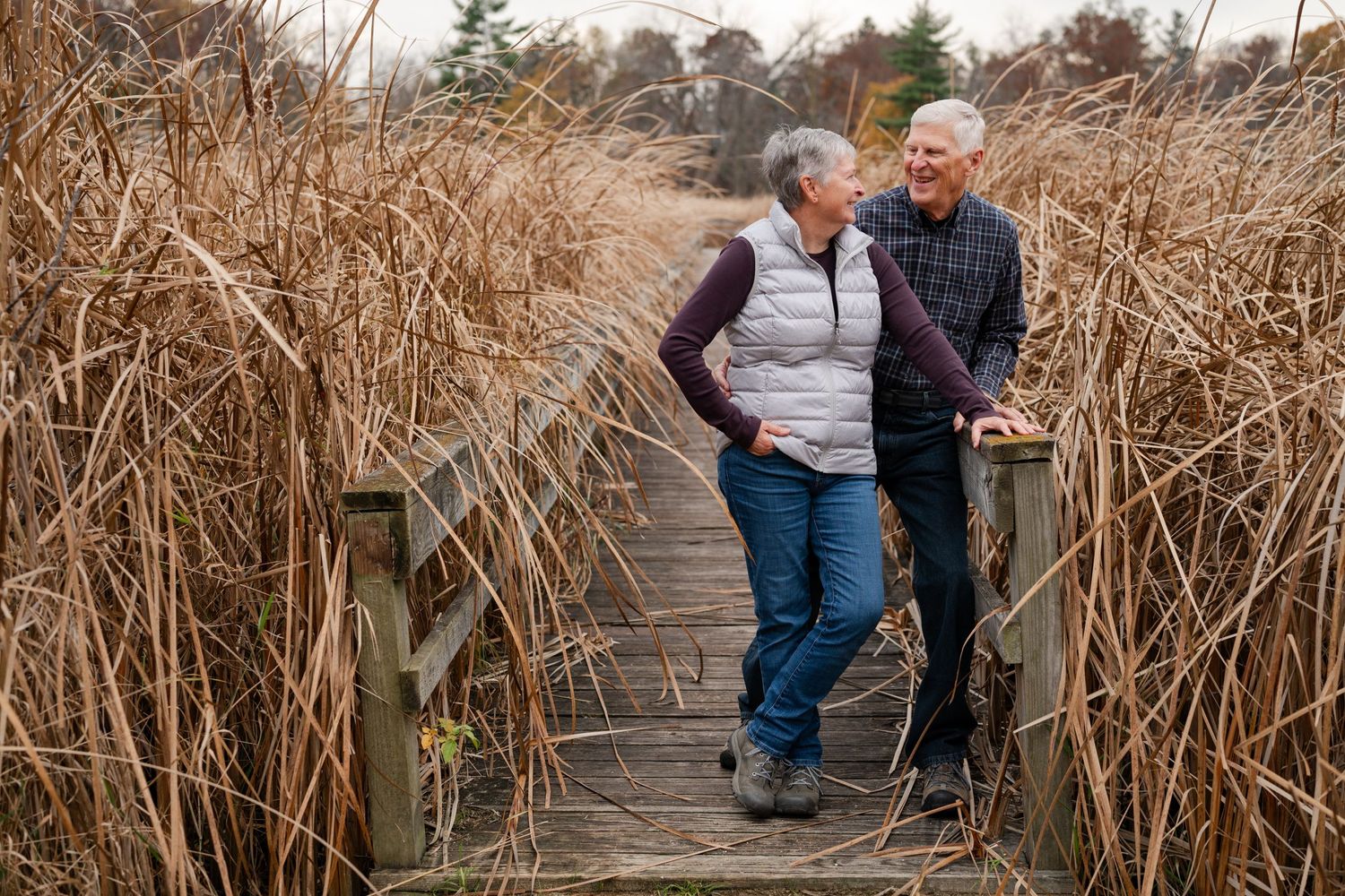 Couple sharing a moment on wooden walkway through tall marsh grasses.