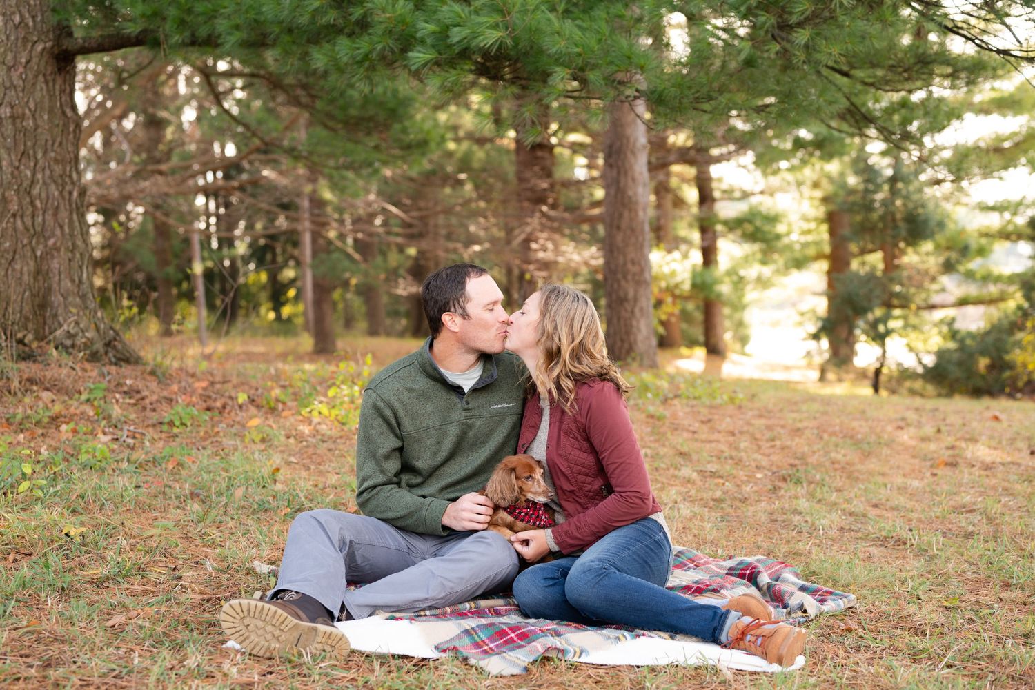 Couple shares intimate moment on plaid blanket in autumn forest setting.