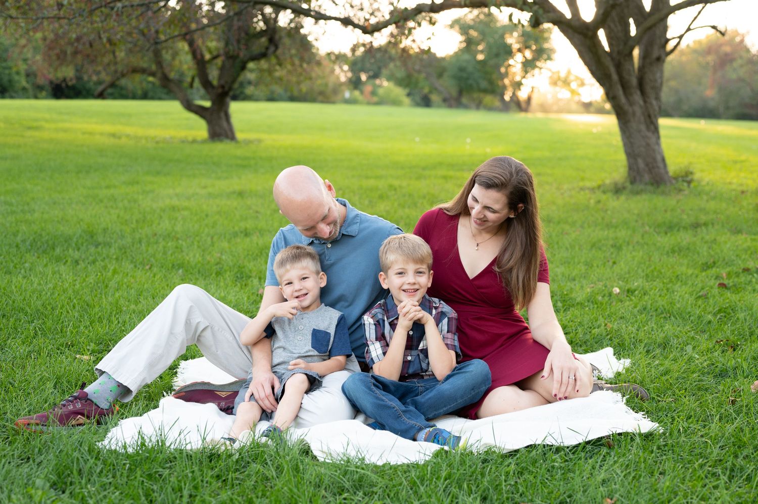 A happy family laughing together while sitting on a blanket in a park.