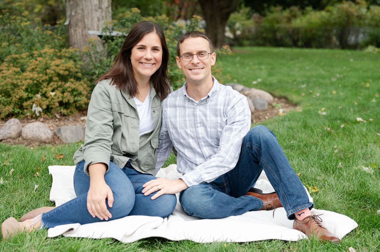 Couple relaxing on white blanket in backyard garden setting.