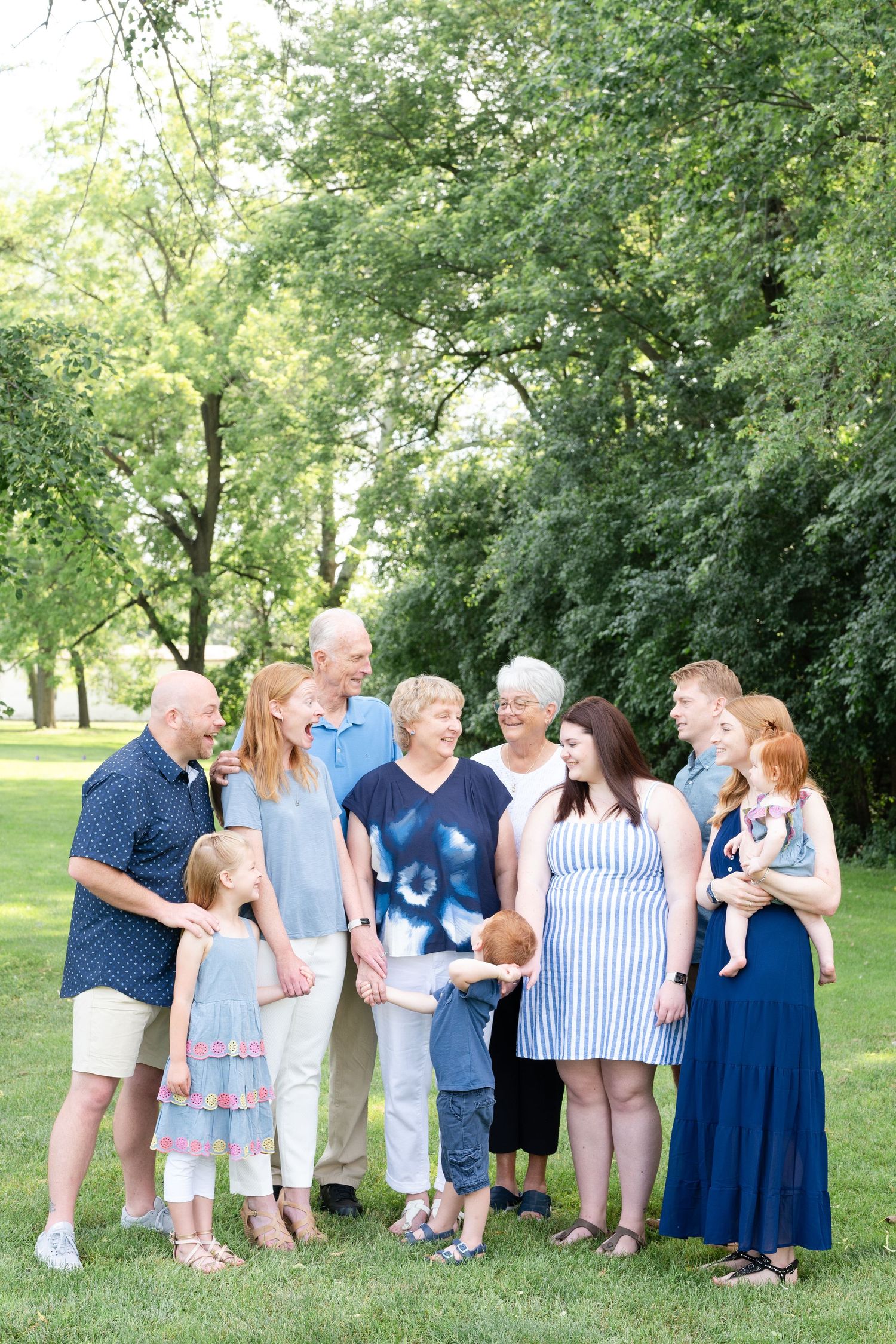 Extended family gathering for a group photo in a park on a sunny summer day.