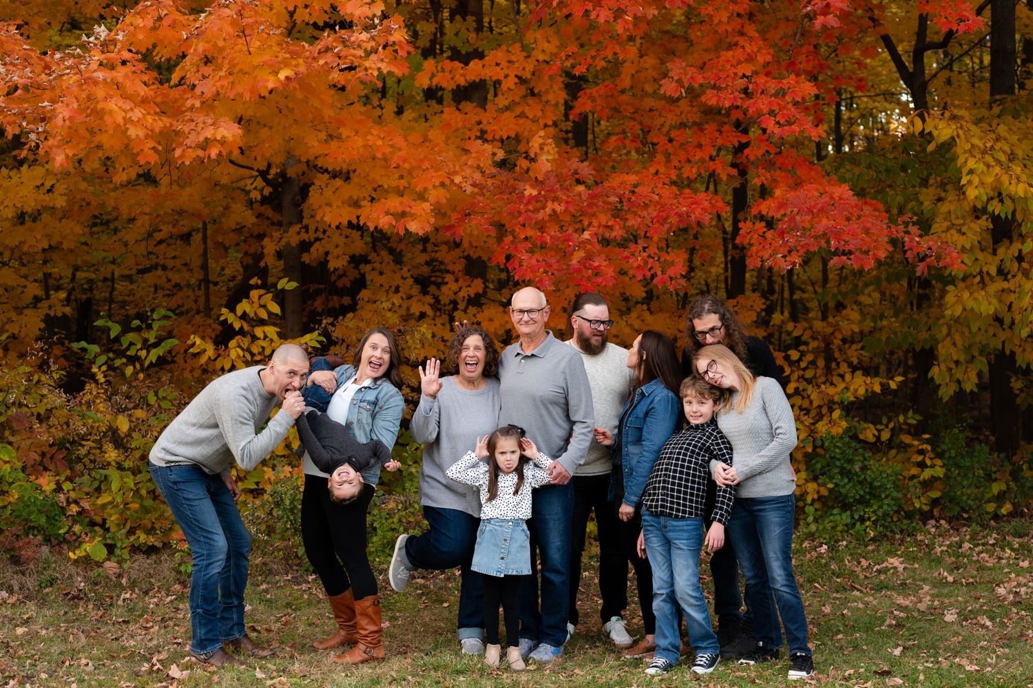 Extended family having fun posing together beneath bright fall maple trees.