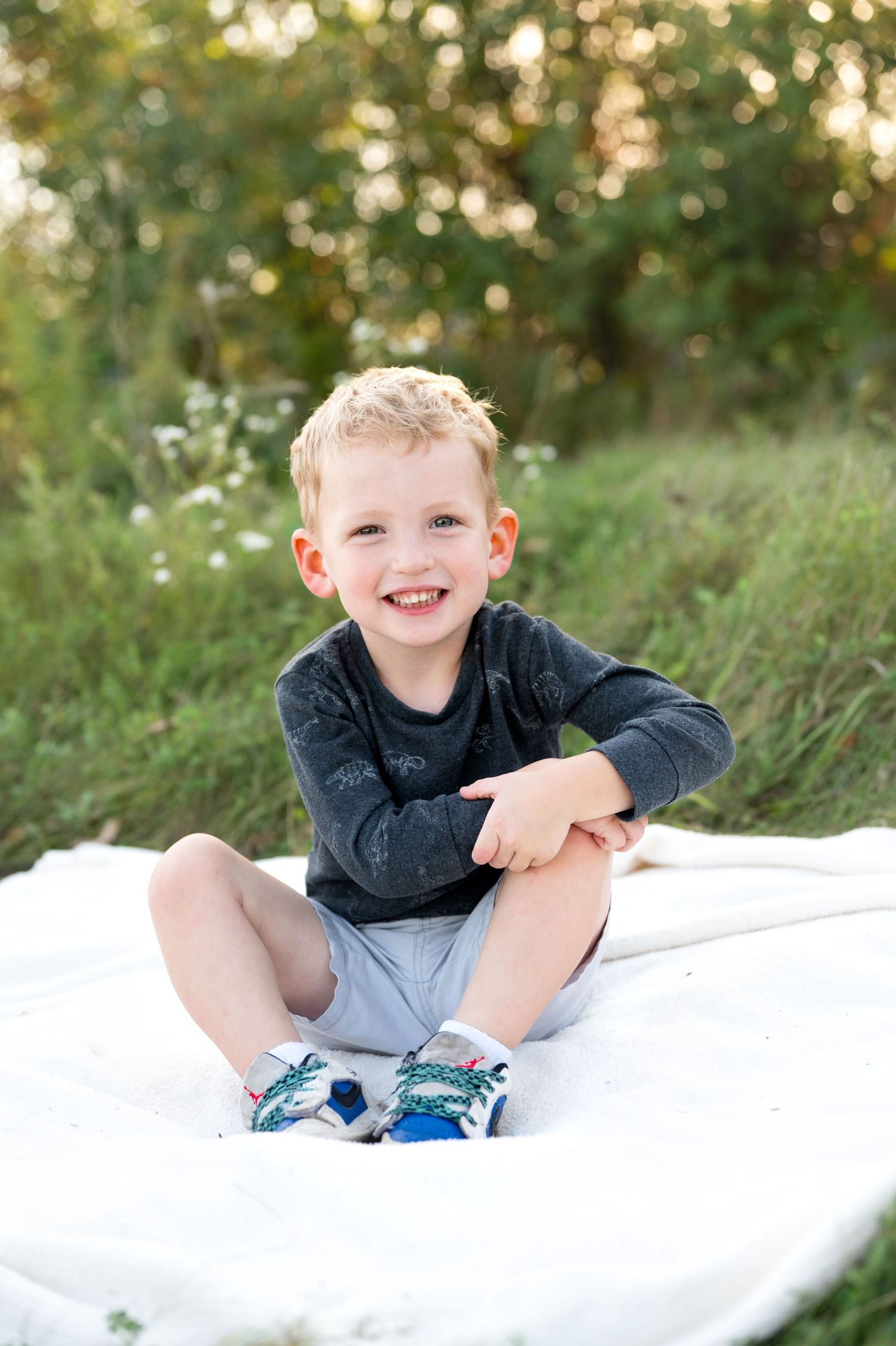 Three candid outdoor photos of a child laying on a white blanket with natural greenery in the background.
