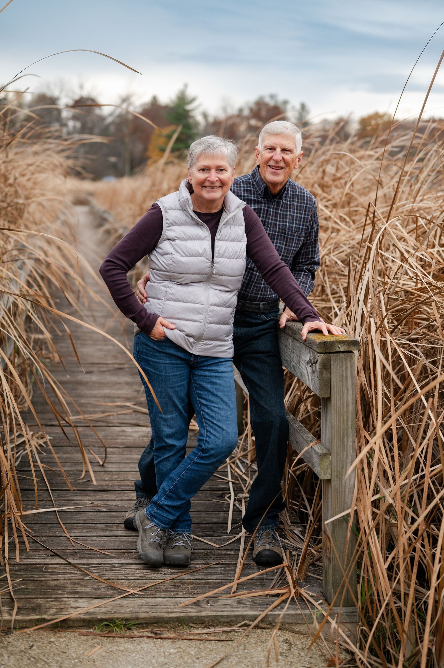 Couple standing on wooden boardwalk surrounded by tall autumn reeds.