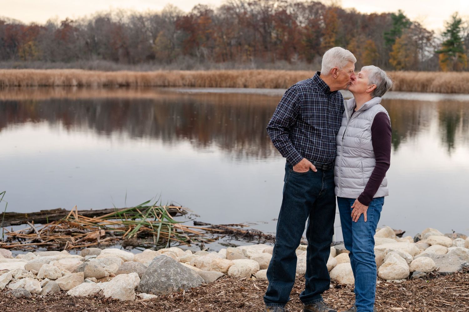 Couple enjoying a peaceful moment by lake shore with autumn foliage in background.