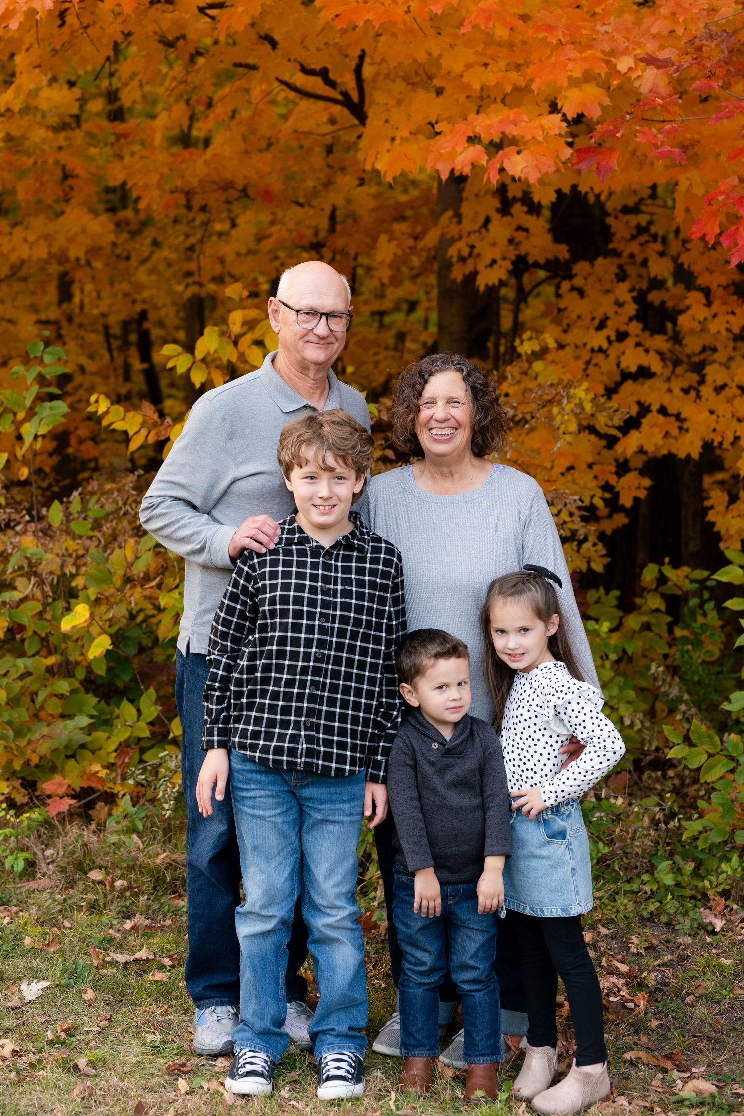 Family portrait outdoors with beautiful autumn foliage creating a colorful orange backdrop.