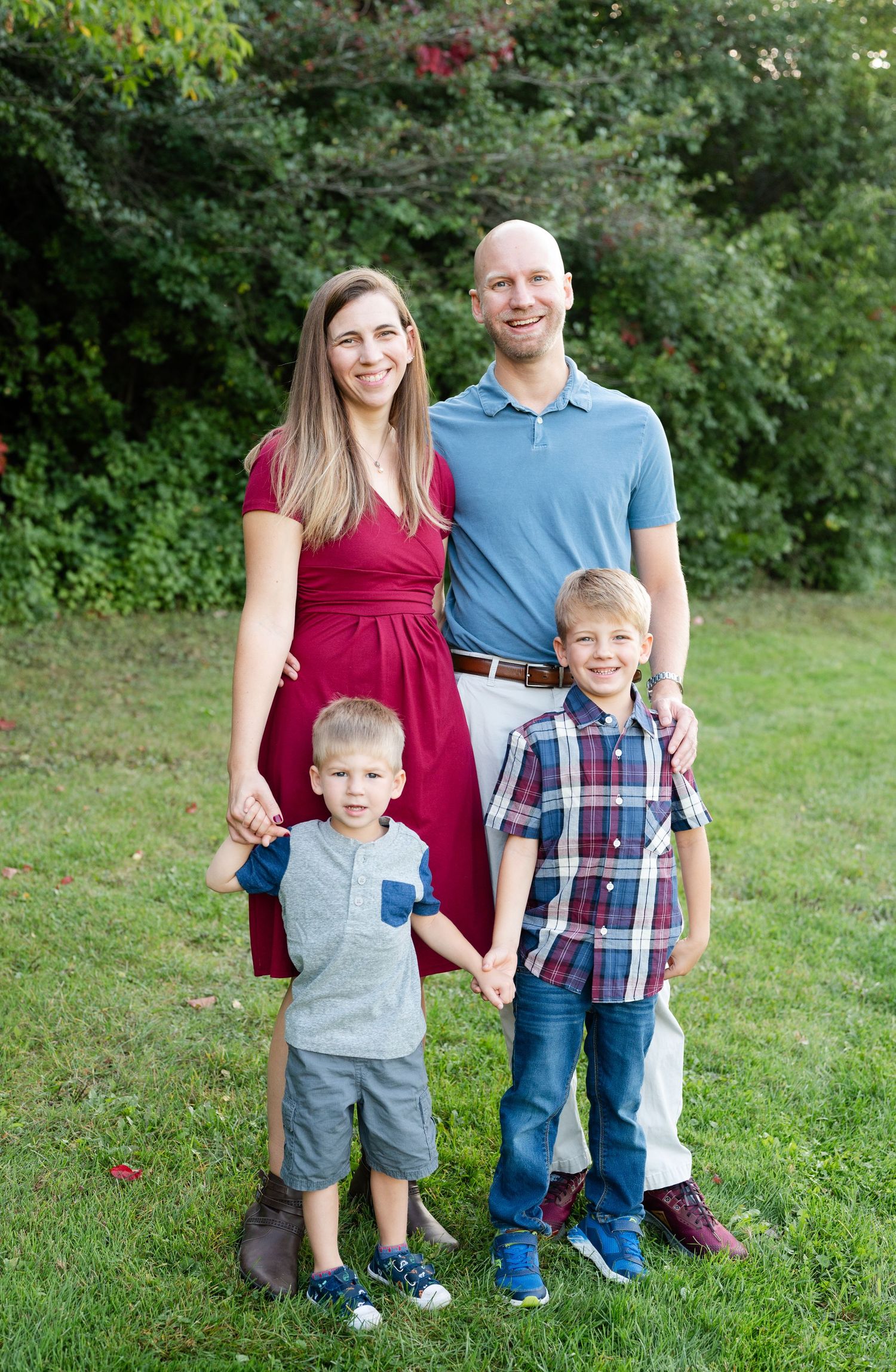 Family of four standing together outdoors in a garden setting with green foliage.