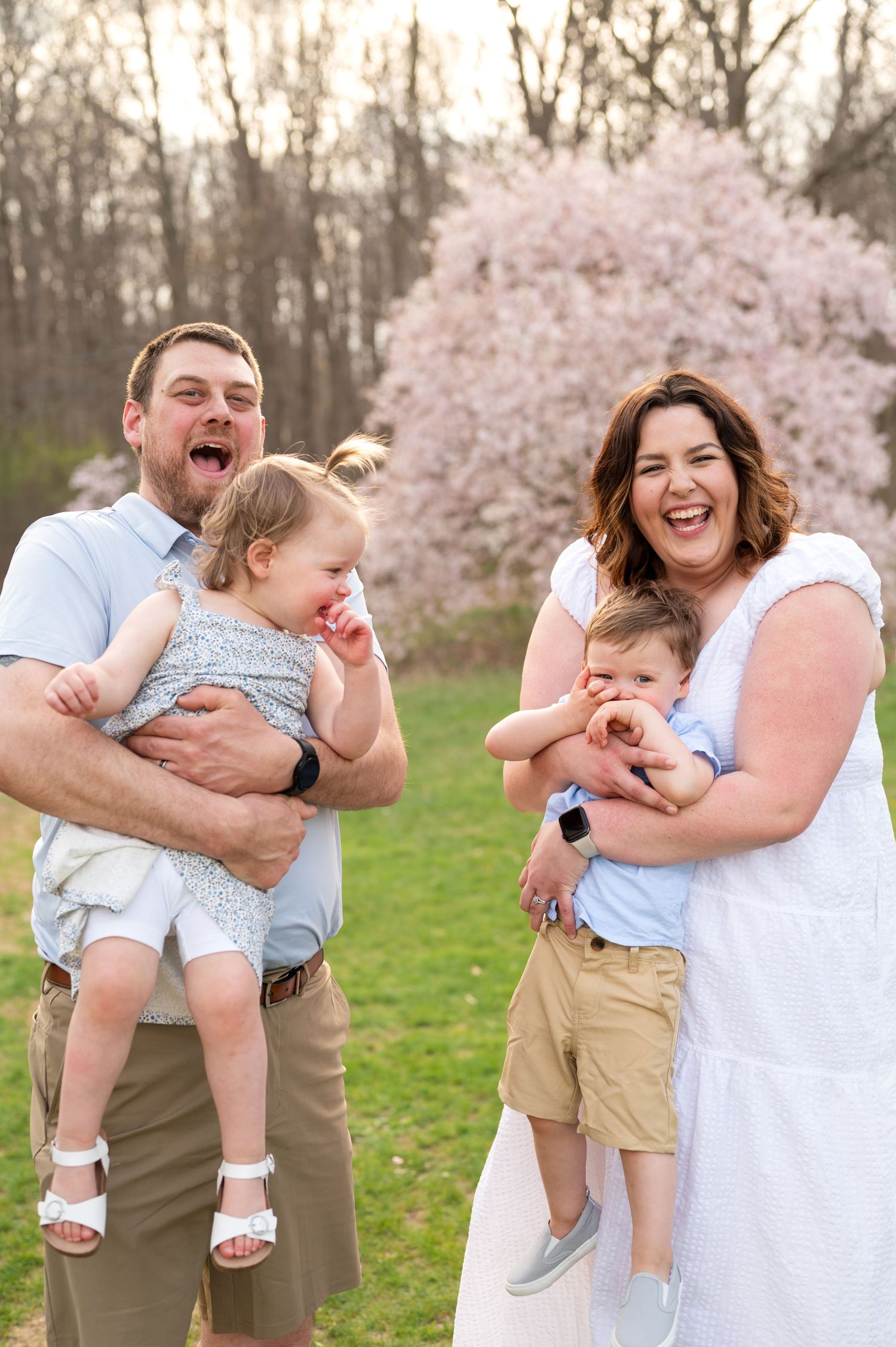 A joyful family laughs together in front of a blooming cherry blossom tree on a spring day.