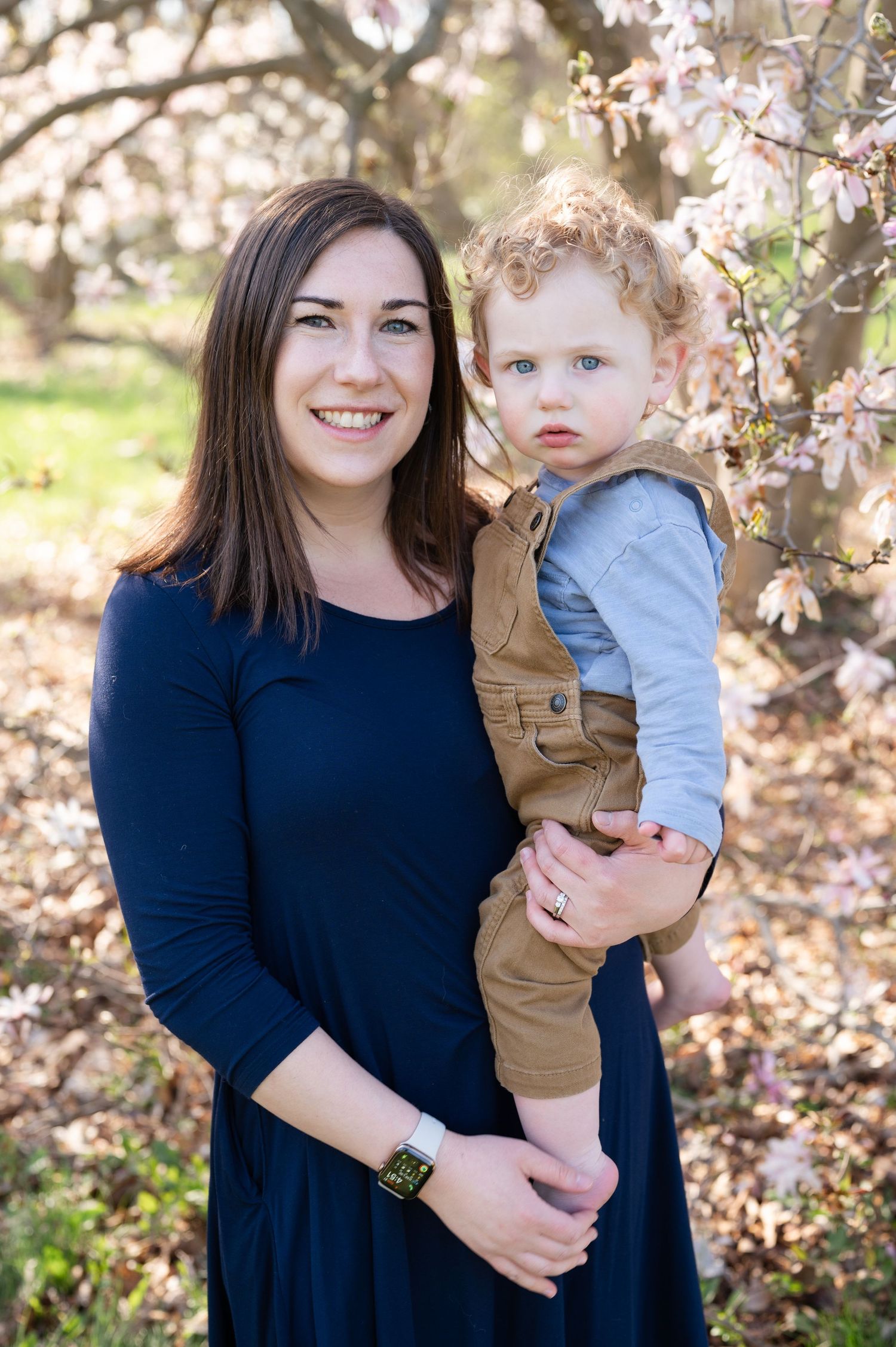 Family portrait featuring spring cherry blossoms with a navy dress and brown overalls against a natural outdoor backdrop.
