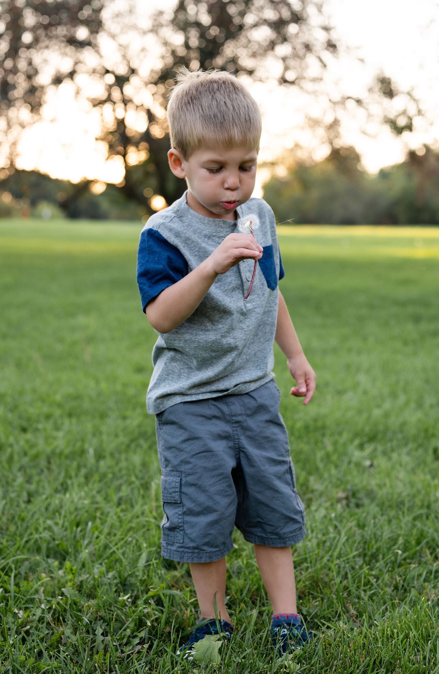 A young boy in casual summer clothes plays in a grassy field at sunset.